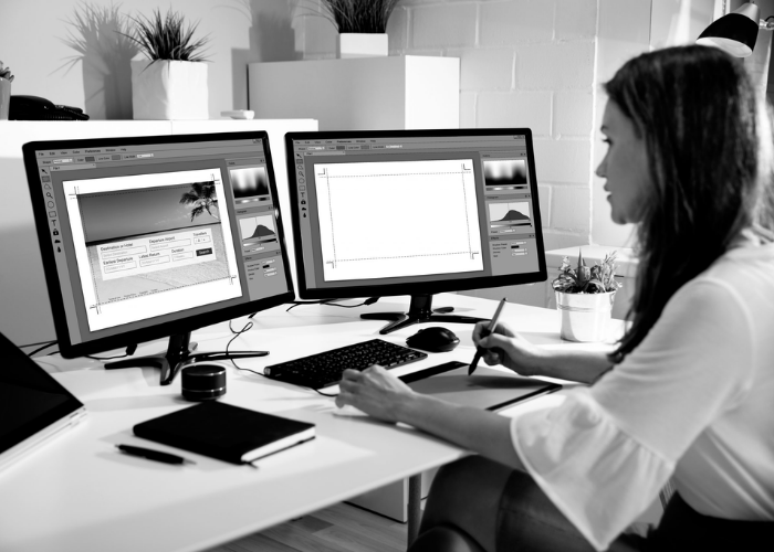 A young woman facing her two desktops publishing content